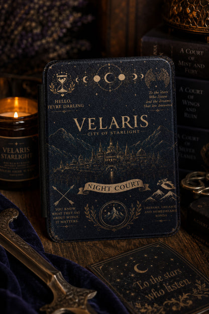 Gold foil Velaris Kindle cover propped on a desk beside a lit candle and Sarah J Maas book spines
