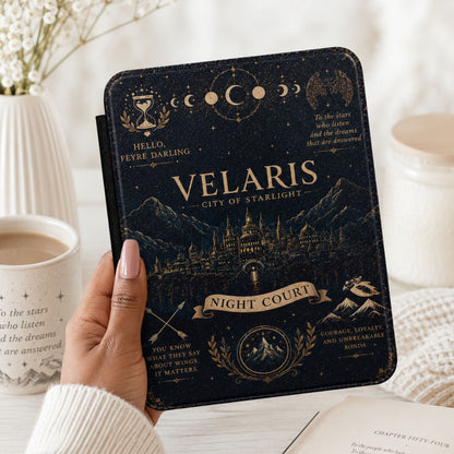 Hand holding a Velaris Kindle case beside coffee, baby's breath flowers, and a cream knit throw
